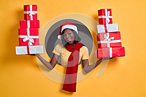 Christmas gift. African American woman in Santa hat and red scarf holding many present boxes posing in a round circle hole in