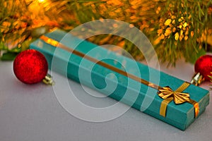 Christmas gift in a blue box with gold ribbon lies under the Christmas tree. red Christmas balls and a beautiful spruce