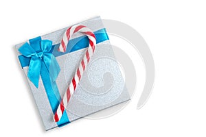 Christmas gift box with blue bow and a red and white candy in form cane on white background