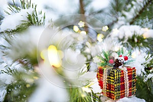 Christmas gift box on a branch of a natural spruce covered with snow. New year outdoor. Snowfall, garland lights, festive mood of