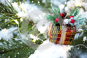 Christmas gift box on a branch of a natural spruce covered with snow. New year outdoor. Snowfall, garland lights, festive mood of