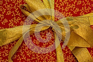 Christmas gift box with a gold ribbon bow on red wrapping paper with gold pattern. Good New Year spirit.