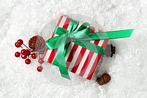 Christmas gift box with green bow and festive decor on snow, flat lay