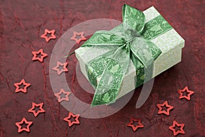 Christmas gift box with green ribbon on a red cloth.