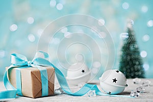 Christmas gift box, jingle bell and blurred fir tree against blue bokeh background. Holiday greeting card.