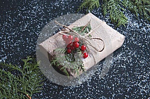 Christmas gift box made of kraft paper with snow on a black table with fir branches