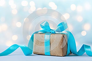 Christmas gift box or present box with beautiful blue ribbon against holiday lights background