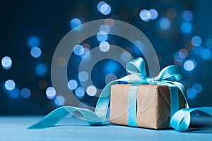 Christmas gift box or present with bow ribbon on magic blue bokeh background. Copy space for greeting card.