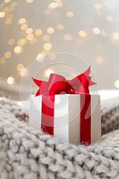 Christmas gift box with red bow on warm knitted sweater and defocused lights