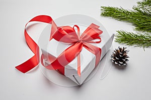 Christmas gift box with red ribbon and green pine tree branch with cones on white