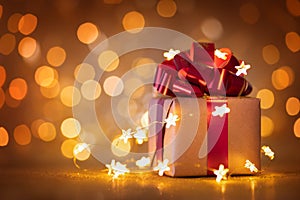 Christmas gift box with red ribbon and lights against golden bokeh background. Holiday greeting card