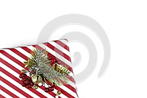 Christmas gift box with red and white striped wrapping paper and seasonal decoration in corner of white background