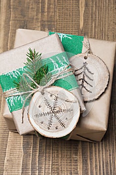 Christmas gift box in rustic style wrapped in paper with decor of wooden sliced with woodburning symbol.