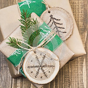 Christmas gift box in rustic style wrapped in paper with decor of wooden sliced with woodburning symbol.