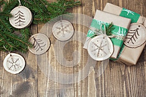 Christmas gift box in rustic style wrapped in paper with decor of wooden sliced with woodburning symbol.