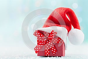 Christmas gift box with Santa hat against turquoise bokeh background. Holiday greeting card.