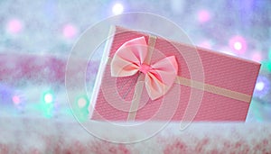 Christmas gift box of soft pink color on a defocused background with burning lights of a garland. Christmas background. Free space