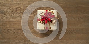 Christmas gift box tied with red and golden bow over a wooden table