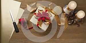 Christmas gift box tied with red and golden bow over a wooden table with candles