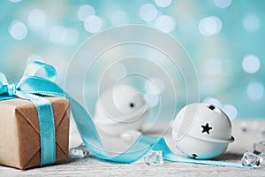 Christmas gift box and white jingle bell against turquoise bokeh background. Holiday greeting card.