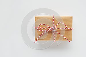 Christmas gift box wrapped in craft paper with red and white striped twine bow on white background. Top view, flat lay, copy space