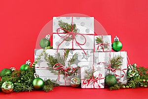 Christmas gift boxes on a red background, decorated of fir branches, pine cones and shiny green Christmas decorations.