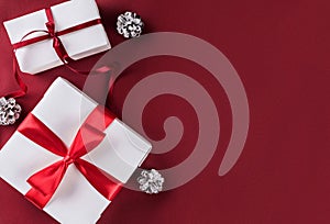 Christmas gift boxes with red ribbon, decoration, pine cones on white and red paper background.