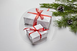 Christmas gift boxes with red ribbon and green pine tree branch with cones on white