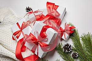 Christmas gift boxes with red ribbon and knitted sweater with green pine tree branch and cones on white