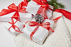 Christmas gift boxes with red ribbon and knitted sweater with green pine tree branch and cones on white