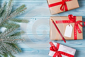 Christmas gift boxes with tag and pencil, fir branch with snow, wooden background, top view