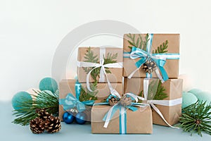 Christmas gift boxes wrapped of craft paper, blue and white ribbons and Christmas lights on the blue and white background.