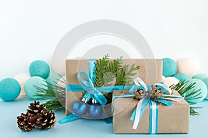 Christmas gift boxes wrapped of craft paper, blue and white ribbons, decorated of fir branches, pine cones and Christmas balls.