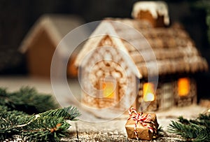 Christmas Gift in Craft Paper with Ribbon next to Gingerbread House. Xmas Present on snowy Dark Background. Ginger House