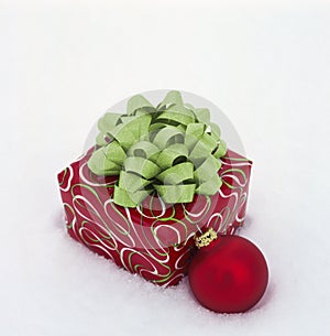 Christmas gift with festive red and green wrapping paper, bow and ornament decoration on white snow background