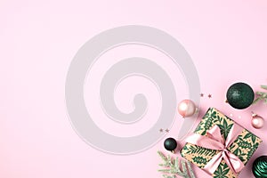 Christmas gift with fir branches and baubles on pastel pink background. Xmas greeting card template