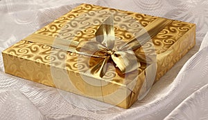 Christmas gift in gold paper with bow on white background