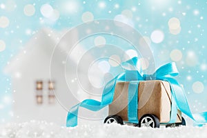 Christmas gift or present box on wheels against turquoise bokeh background. Holiday greeting card with snow effect.