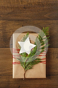 Christmas gift present with recycled wrapping paper, blank gift tag and natural evergreen decorations on rustic wood background