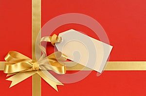 Christmas gift red background, gold ribbon bow, gift tag, copy space