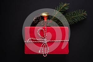 Christmas gift in red paper decorated with spruce twigs, pine cone, bell