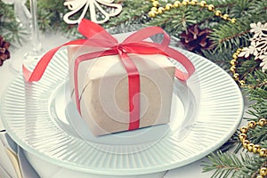Christmas gift with red ribbon on cyan plate with fir-tree branches on white wooden table.