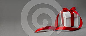 Christmas Gift in White Box with Red Ribbon on Dark Grey Background. New Year Holiday Composition Banner. Copy Space For Your Text