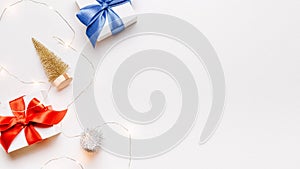 Christmas gift. White gift with red bow, gold balls and sparkling lights garland in xmas decoration on white background