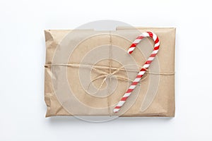 Christmas gift wrapped in craft paper, tied with scourge, decorated with cane candy on white background. Simple minimal style.