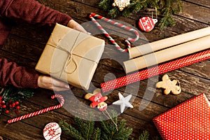 Christmas gift wrapped in eco paper being held on wooden background alongside cookies with winter holidays festive shapes, candy