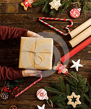 Christmas gift wrapped in eco paper being held on wooden background alongside cookies with winter holidays festive shapes, candy
