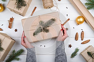 Christmas gift wrapping background. Female hands packaging christmas present wrapped in kraft paper, top view.