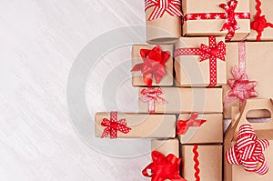 Christmas gifts background - various craft paper gifts with red ribbons and bows on soft light white wood board, flat lay.