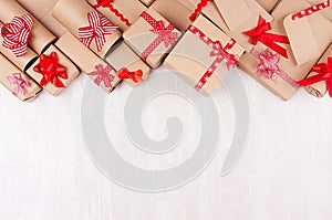 Christmas gifts background - various craft paper gifts with red ribbons and bows, blank label on soft light white wood board.